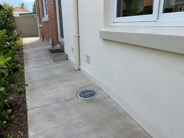 Concrete side path beside a brick and rendered house with a drain grate in place in Brighton-Le-Sands