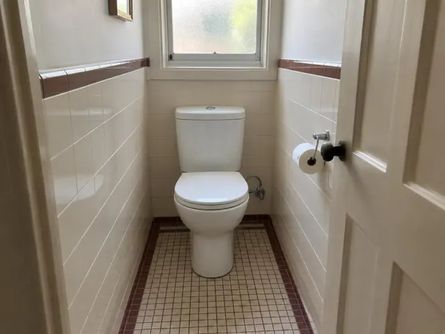 Clean white toilet in a tiled small bathroom with frosted window in Arncliffe