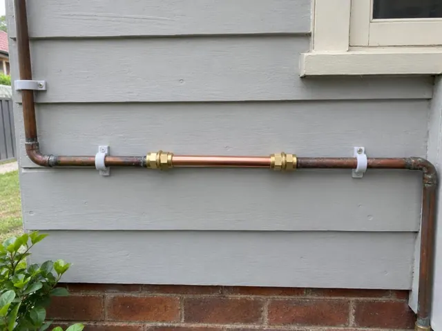 Repaired copper water pipe mounted on grey weatherboard exterior wall beside a window in Rockdale