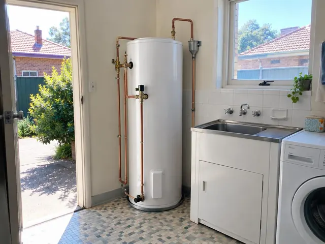White hot water cylinder beside a laundry sink in a tiled utility room in Kogarah