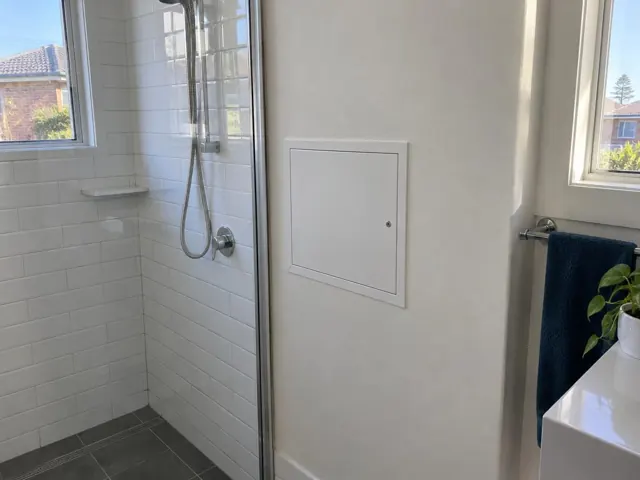 White access panel on a bathroom wall beside a shower and tiled shower recess in Rockdale